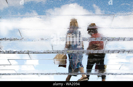 Reflexion Schatten Silhouetten der beiden Frauen zu Fuß auf einer nassen Straße an einem sonnigen Sommertag in der Stadt Stockfoto