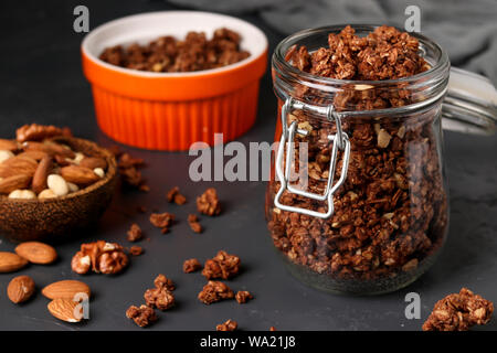 Müsli knuspriges Müsli mit natürlichem Honig, Schokolade und Nüsse in einem Glas vor einem dunklen Hintergrund, gesundes Essen, Nahaufnahme, horizontale Ausrichtung Stockfoto