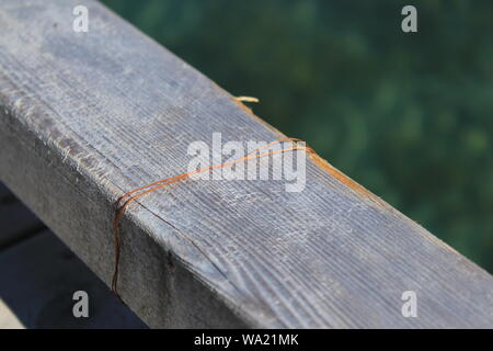 In der Nähe von eine Alte verrostete Kabel an ein Brett aus Holz mit Wasser im Hintergrund befestigt Stockfoto