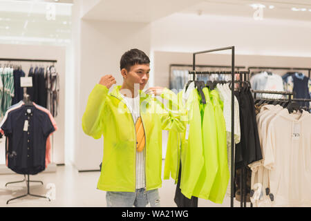 Bangkok, Thailand - 19. Mai, 2019: Ein junger Mann versucht, auf einem semi-transparente neon Jacke von fluoreszierenden Kalk Farbe in einer ZARA Store. Stockfoto