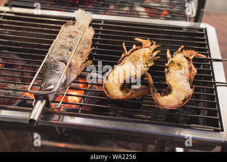 Gegrillter Fisch und Langusten liegen auf dem Holzkohlegrill über die rote Glut. Eine Nahaufnahme, geringe Tiefenschärfe. Stockfoto