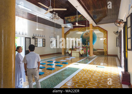 Tempel Attendant (links) & unbekannter Mann unterhalten vor der Sphäre der linken Auge Gottes in Trung Hung Buu Toa Cao Dai, ein Caodaist Tempel in Da Nang. Stockfoto