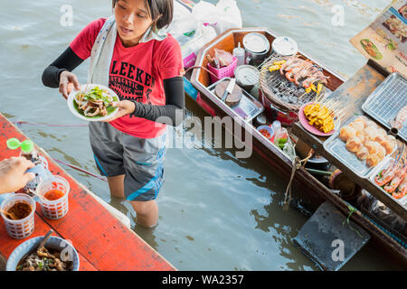 Amphawa, Thailand: ein Mädchen, die sich für schwimmende Garküche, dient die Platte mit gegrilltem Tintenfisch (120 Baht), mit Ihrem Boot hinter am schwimmenden Markt Amphawa Stockfoto