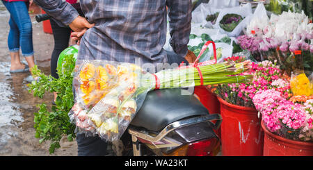 Ho Thi Ky Blumenmarkt in Ho Chi Minh City (Saigon), Vietnam: ein Strauß Blumen auf einem Roller Sitz hinter einem Mann in der Nähe von Eimern mit Blumen. Stockfoto