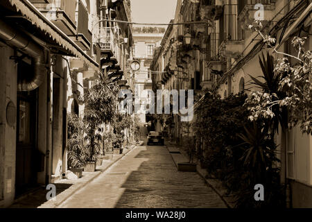 Typische italienische Straße in Catania. Gepflasterte Straße mit wenig Bäume und Häuser mit kleinen Balkonen auf beiden Seiten. Schwarz und Weiß Stockfoto