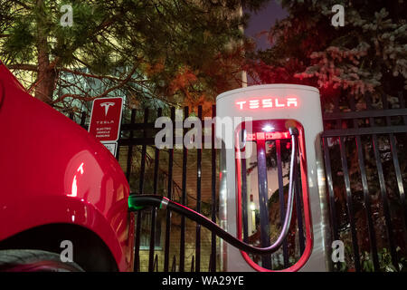 Tesla Kompressor bei Nacht mit roten Tesla Fahrzeug gesteckten, Laden gesehen. Stockfoto