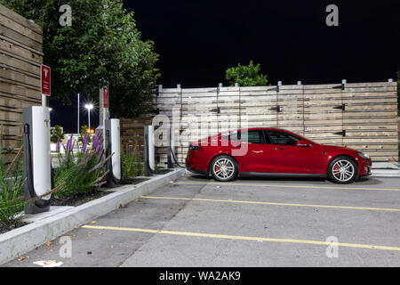 Red Tesla Model S laden bei Tesla Kompressor unter helle Lichter in der Nacht. Stockfoto