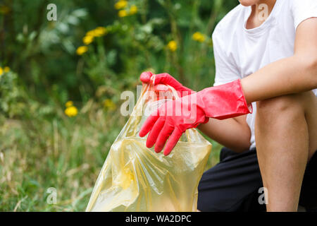 Junge im weißen T-Shirt in Handschuhen sammelt Müll- und Plastikflaschen in blauen Paket am Strand. Junge Freiwillige. Umweltschutz Stockfoto