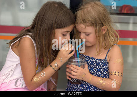 Zwei kleine Mädchen, das Trinken aus dem gleichen Kelch mit zwei strohhalme Stockfoto