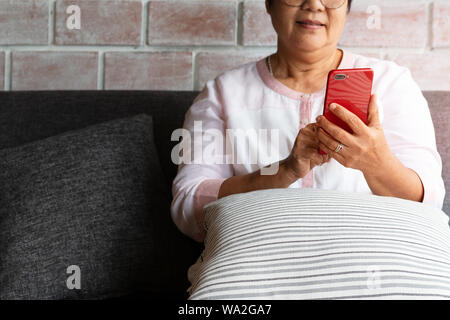 Ältere Frau mit Mobiltelefon von Sofa zu Hause sitzen Stockfoto