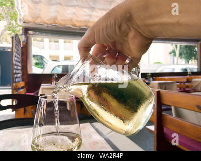 Nahaufnahme einer Hand gießen Weißwein aus einer Kanne in der Wineglass, Außenaufnahme Stockfoto