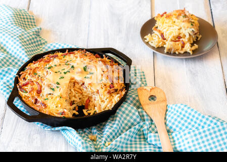 Deutsches Essen, Spätzle mit Speck und geschmolzenem Käse in einem Guss Pfanne auf einem bayerischen Handtuch, auf einem weißen Tisch. Schwäbische Teller Nudeln mit Ei und Käse Stockfoto