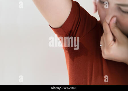 Frau mit Hyperhidrose schwitzen. Junge Asien Frau mit Schweiß Fleck auf ihrem Unterarm Kleidung. Healthcare Konzept Stockfoto