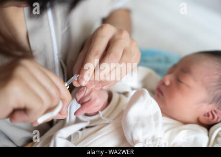 Asiatische Babys erste Fingernägel schneiden, während seine Mutter mit einer Schere zu schlafen. Nahaufnahme Krankenpflege ein Kind. Wie man erfolgreich clip Nägel Ihr Baby. Stockfoto