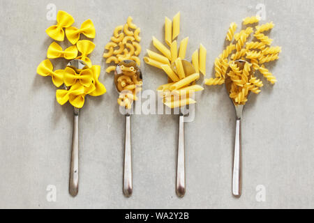 Verschiedene Arten von Nudeln in Löffel auf grauem Hintergrund. Vielzahl von Pasta, italienische Küche. Stockfoto
