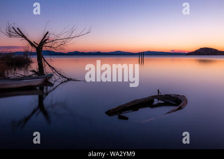 Eine fast vollständig versenkt kleines Boot in See Trasimeno (Umbrien, Italien) in der Abenddämmerung, in der Nähe von einem Skelett Baum Stockfoto