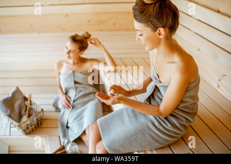 Zwei junge Freundinnen entspannen in der Sauna, zusammen zu sitzen und die nicht für sich selber sorgen. Konzept der weiblichen Freundschaft und Kur Stockfoto