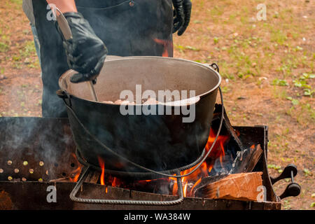 Küche bei Party Picknick geöffnet. Pilav Kochen am Feuer im Freien. Koch Koch ist das rühren Mahlzeit Teller in den großen Topf von Kelle. Bushpot bleibt auf Draht Rack und s Stockfoto