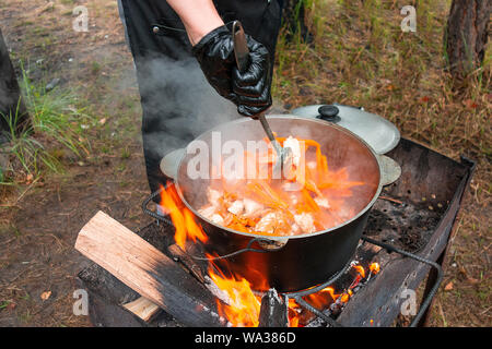 Küche bei Party Picknick geöffnet. Pilav Kochen am Feuer im Freien. Koch Koch ist das rühren Mahlzeit Teller in den großen Topf von Kelle. Bushpot bleibt auf Draht Rack und s Stockfoto