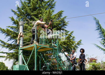 Eine junge kenianische Frau reisen auf einem Zip Line mit Hilfe von Guide im Forest Recreation Center, Kenia Stockfoto