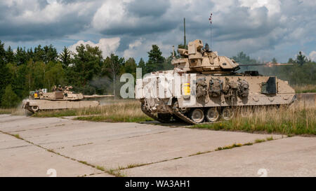 Ein M1 Abrams Tank vom 3. Battalion, 66th Panzer Regiment und einer M2 Bradley fighting Fahrzeug, das Eigentum der 1. Techniker Bataillon, 1st Armored Brigade Combat Team, 1.Infanterie Division, gleichzeitig an verschiedene Ziele während einer kombinierten Waffen Ausbildung Szenario auf eine Reihe an grafenwöhr Training Area, Germany, August 8, 2019. Diese Übung ist die 1 ABCT die letzte Veranstaltung vor der Teilnahme an kombinierten Lösen XII. (U.S. Armee Foto: Staff Sgt. Adam Decker) Stockfoto