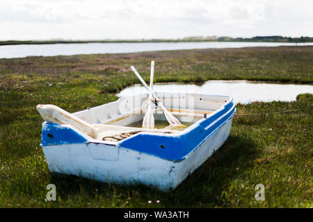 Ein Strände blaue und weiße Ruderboot auf der grünen Wiese Sumpfland in Orford, Suffolk Stockfoto