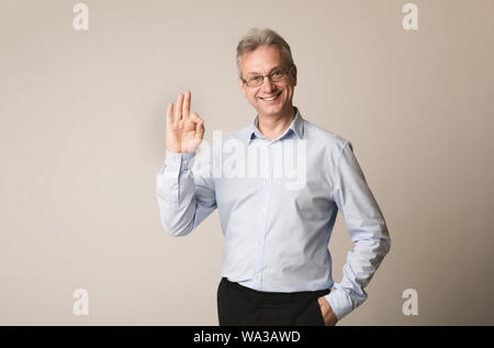 Senior Geschäftsmann, okay Geste, grauer Hintergrund Stockfoto