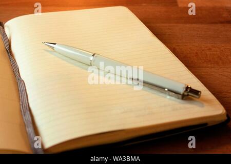 Nahaufnahme eines weißen Stifts auf einem offenen leeren Notizbuch Stockfoto