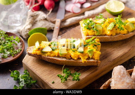 Bio Rührei auf rustikale französische Baguette mit frischen Kräutern und Avocado Stockfoto