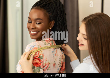 Junge weibliche Schneiderin die Körpermaße des Kunden in Fashion showroom Stockfoto