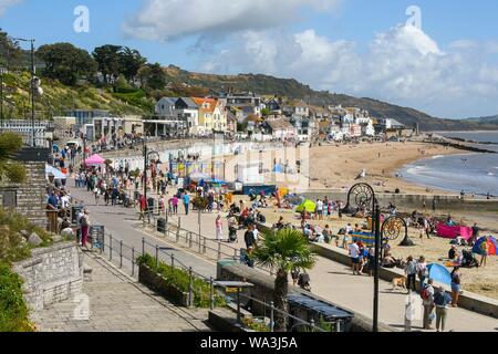 Lyme Regis, Dorset, Großbritannien. 17. August 2019. UK Wetter. Urlauber zu Fuß entlang der Strandpromenade als Sonnenanbeter zurück zum Strand nach dem gestrigen Regen in den Badeort Lyme Regis in Dorset an einem warmen sonnigen. Foto: Graham Jagd-/Alamy leben Nachrichten Stockfoto