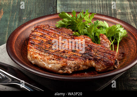 Auf einer hölzernen Tisch auf einem weißen Teller liegt ein Stück gebratenes Schweinefleisch mit Kräutern, Detailansicht Stockfoto