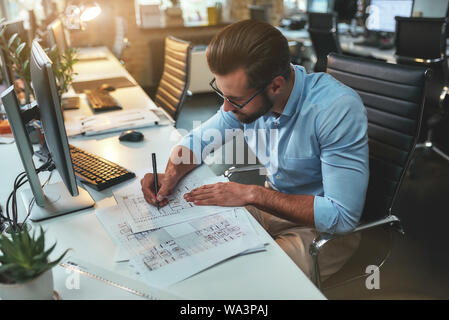 Architektonisches Projekt. Erfolgreich besetzt bärtigen Mann in Brillen und Gesellschaftsmode Zeichnung etwas während der Arbeit im Büro. Ingenieur. Bau plan Stockfoto