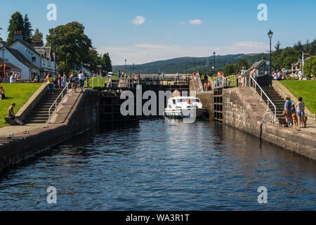 Ein Boot macht seinen Weg durch Schleusen auf dem Caledonian Canal an Fort Augustus, in der Nähe von Loch Ness in Schottland an einem sonnigen Tag, von Touristen beobachtet. Stockfoto