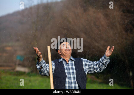 Bauer im Regen, die Arme offen und zufrieden Stockfoto