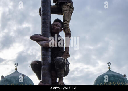 Lhokseumawe, Aceh, Indonesien. 17 Aug, 2019. Der Teilnehmer trägt das Gewicht von anderen Männern, wie sie versuchen, die Preise in eine gefettete-Pole Climbing Wettbewerb als Teil der gefeierten Indonesien 74th Tag der Unabhängigkeit in Lhokseumawe zu erreichen. Indonesien die Unabhängigkeit von der niederländischen Kolonialismus in 1945 und jetzt 2019 ist der 74. Jahrestag der Unabhängigkeit von Indonesien. Credit: zikri Maulana/ZUMA Draht/Alamy leben Nachrichten Stockfoto