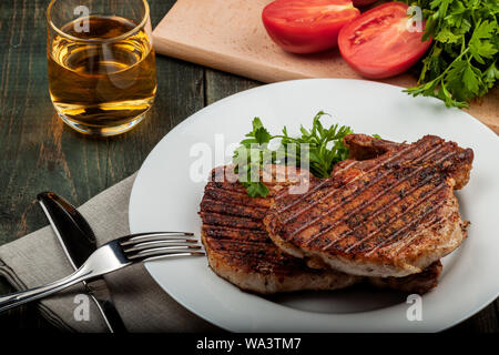 Auf einer hölzernen Tisch auf einem weißen Teller liegt zwei Stücke gebratenes Schweinefleisch mit Kräutern, Detailansicht Stockfoto