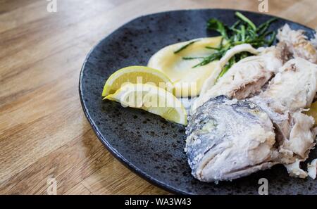 Nahaufnahme eines rohen Fisches mit Zitronen auf einer Runde Platte Stockfoto