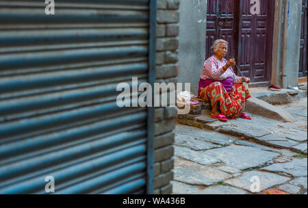 Lächelnd asiatischen älterer Frauen sitzt auf einem Bürgersteig und ist Spinnen von Wolle Stockfoto