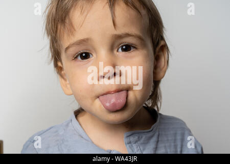 Glückliches Kind, seine Zunge auf weißem Hintergrund. Super nette junge Junge. Stockfoto