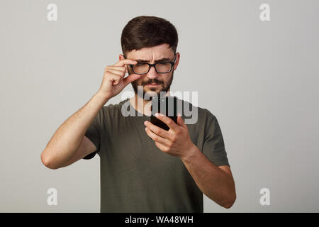 Ein junger Kerl schaut in das Handy mit seinen Augen verengten sich. Nichts sieht Stockfoto