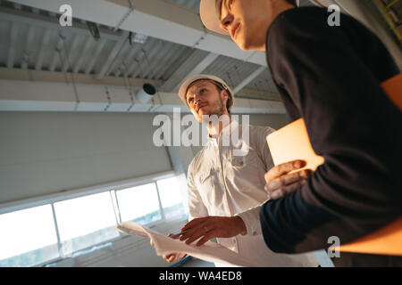 Zwei Bauingenieure mit blueprint Arbeiten auf der Baustelle. Industrielle enginer und Arbeiter auf der Suche Zeichnung Stockfoto