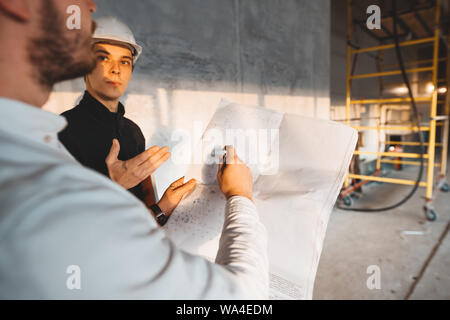 Gebäude, Techniker und Arbeiter halten Blaupause in der Hand während discussong Baustelle. Industrielle haben die Ingenieure am Bau Stockfoto