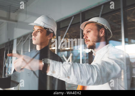 Gebäude, Techniker und Arbeiter halten Blaupause in der Hand während discussong Baustelle. Industrielle haben die Ingenieure am Bau Stockfoto