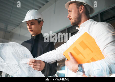 Gebäude Arbeiter und Architekten diskutieren Zeichnung auf der Baustelle. Zwei Wirtschaftsingenieure tragen Sicherheit harten Hut haben Tagung am commerci Stockfoto