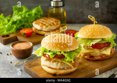 Zwei selbstgemachte Burger mit Schnitzel Hähnchen Fleisch, Käse, Tomaten und Speck auf einem Holzbrett. Stockfoto