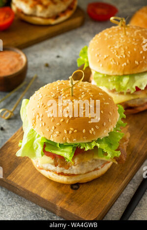 Zwei selbstgemachte Burger mit Schnitzel Hähnchen Fleisch, Käse, Tomaten und Speck auf einem Holzbrett. Stockfoto