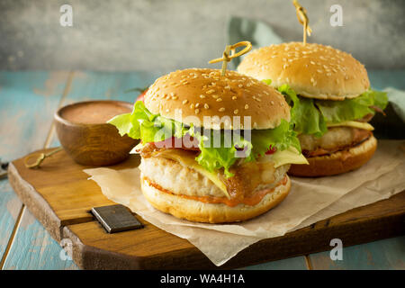 Zwei selbstgemachte Burger mit Schnitzel Hähnchen Fleisch, Käse, Tomaten und Speck auf einem Holzbrett. Freier Platz für Ihren Text. Stockfoto