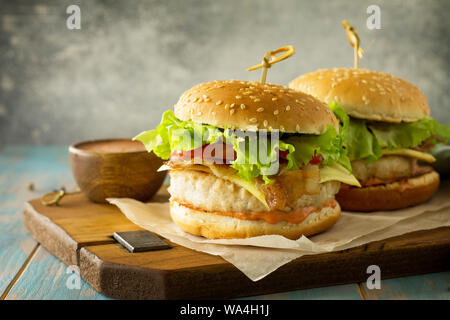 Zwei selbstgemachte Burger mit Schnitzel Hähnchen Fleisch, Käse, Tomaten und Speck auf einem Holzbrett. Freier Platz für Ihren Text. Stockfoto