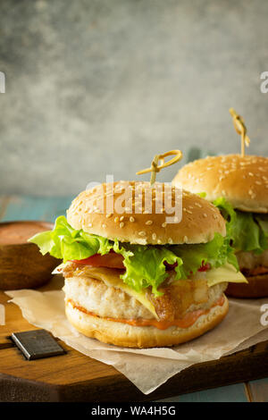 Zwei selbstgemachte Burger mit Schnitzel Hähnchen Fleisch, Käse, Tomaten und Speck auf einem Holzbrett. Freier Platz für Ihren Text. Stockfoto